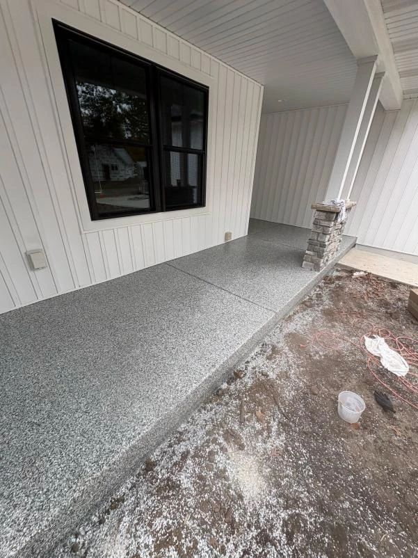 Newly coated covered porch floor with a gray flake finish on a white farmhouse