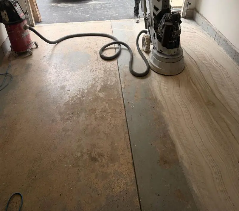 Diamond grinder removing an old garage floor coating, with ground concrete on one side and the old floor on the other