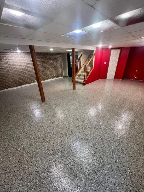 Gray flake floor coating in a finished basement with a red accent wall and a staircase