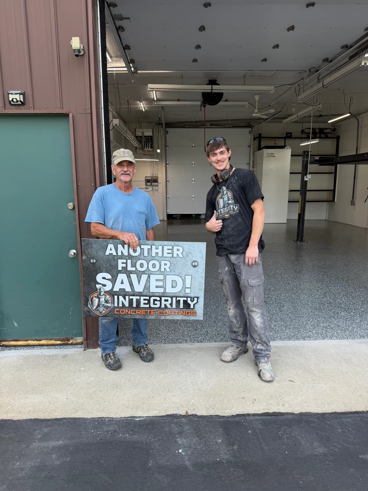 Homeowner and Integrity crew member holding an Another Floor Saved sign in a finished shop garage