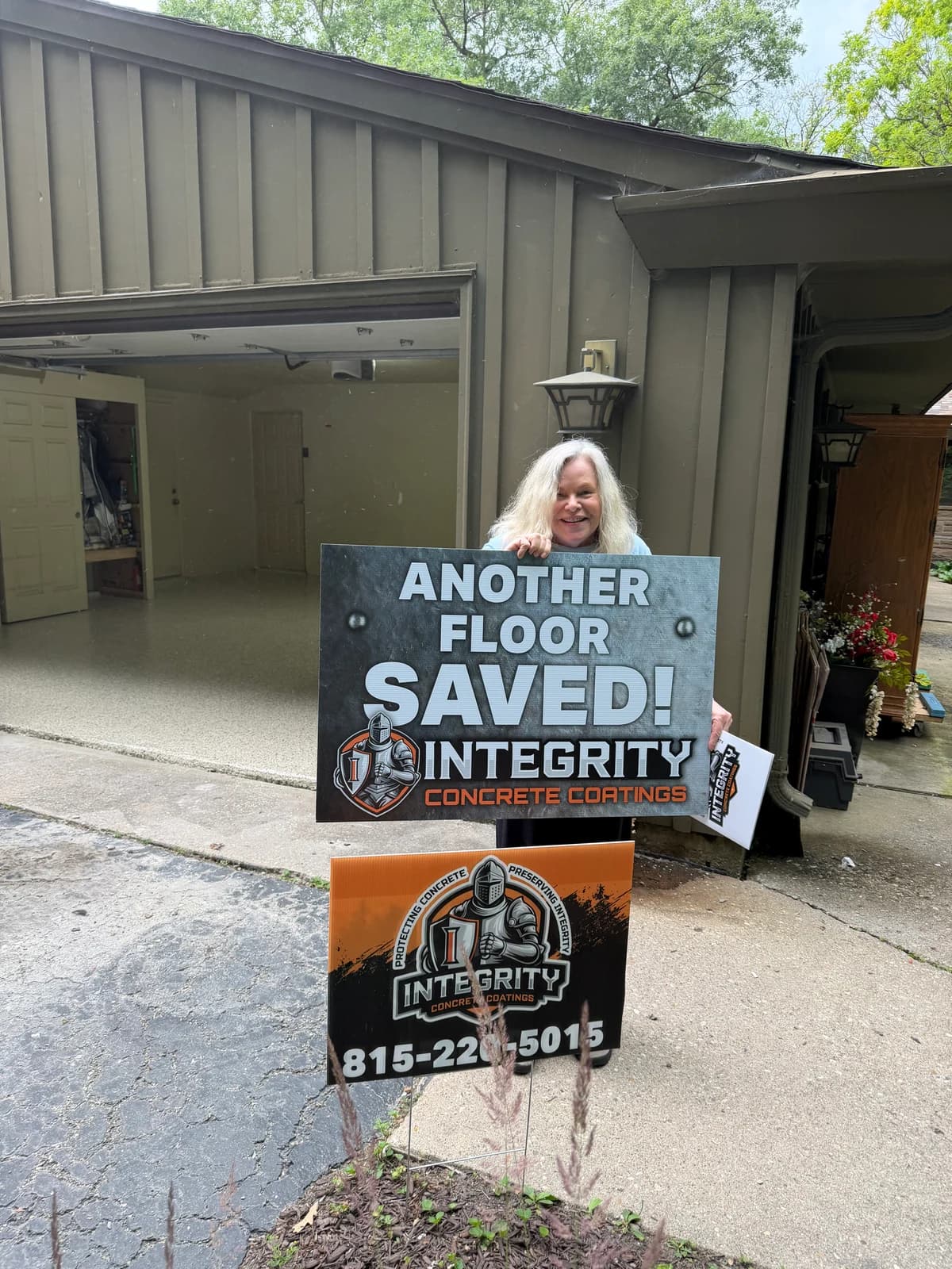 Customer holding an Another Floor Saved sign in front of a coated garage floor