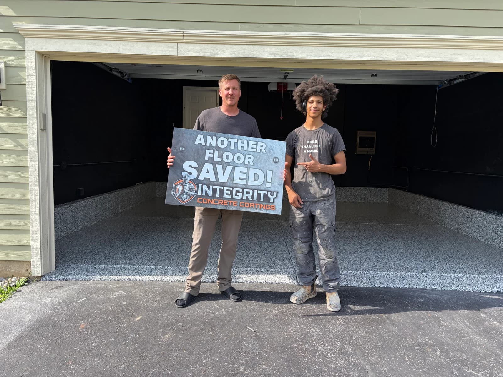 Crew member and homeowner holding an Another Floor Saved sign at a freshly coated garage