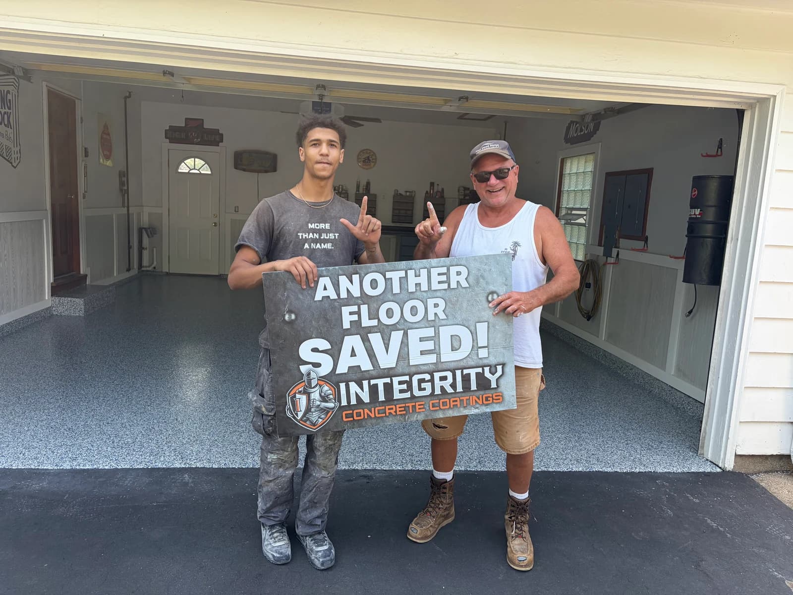 Crew member and homeowner holding an Another Floor Saved sign in a coated garage