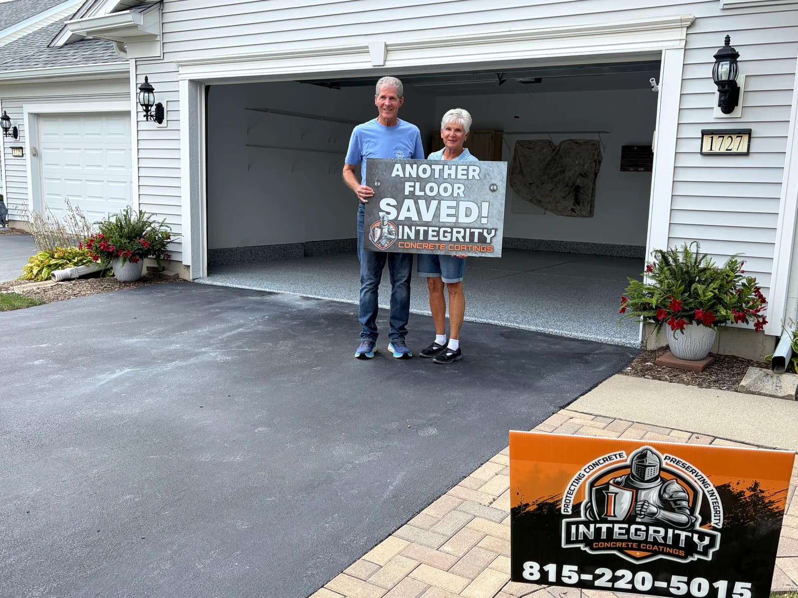 Homeowners holding an Another Floor Saved sign on the driveway of a coated garage