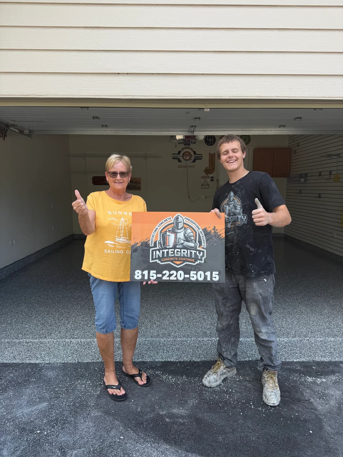 Integrity crew member and homeowner with a company sign in front of a newly coated garage floor
