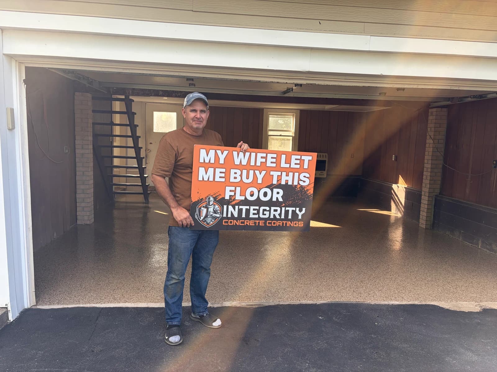 Customer holding a My Wife Let Me Buy This Floor sign in front of a coated garage floor