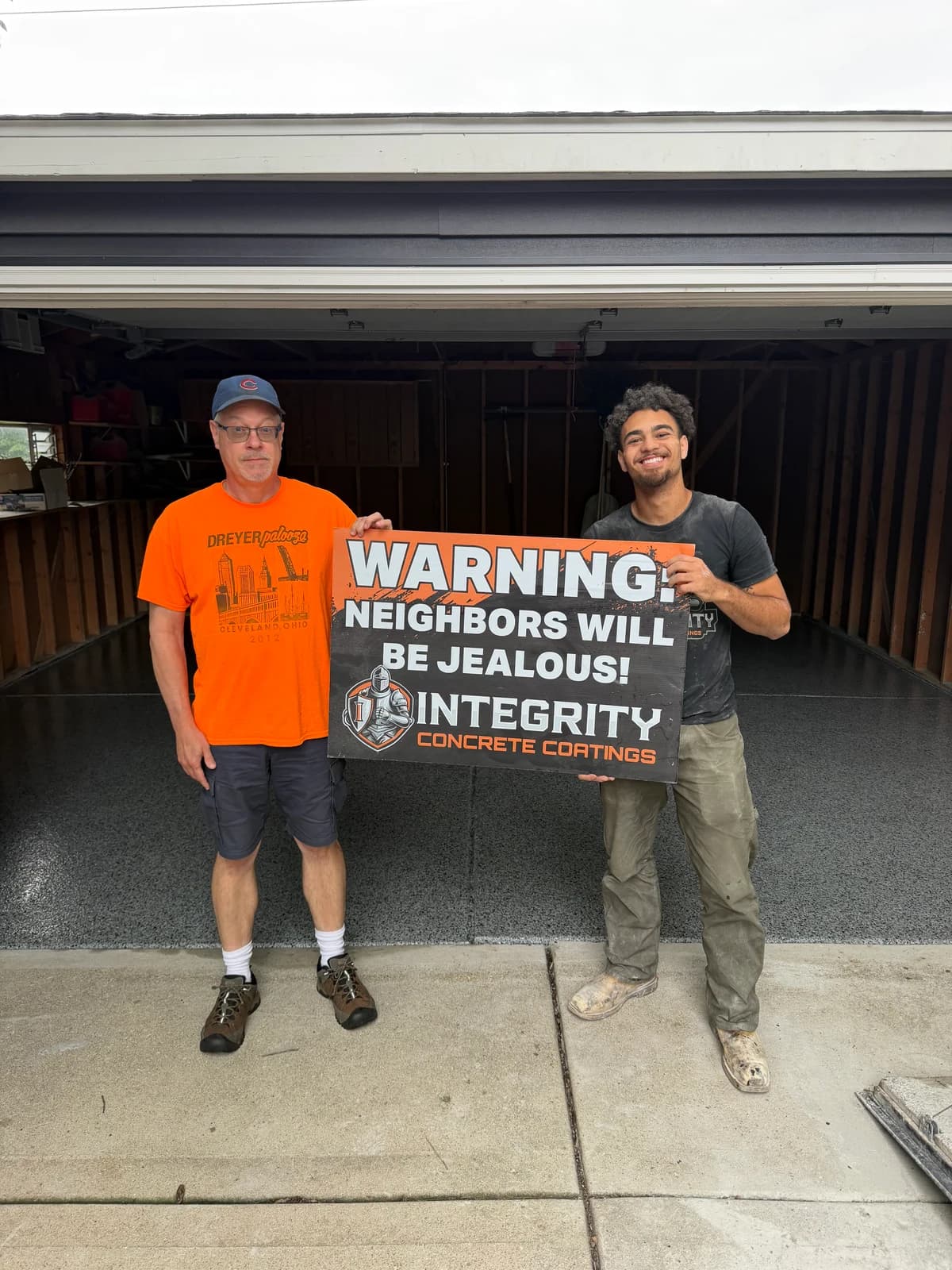 Homeowner and crew member with a Neighbors Will Be Jealous sign beside a coated garage floor