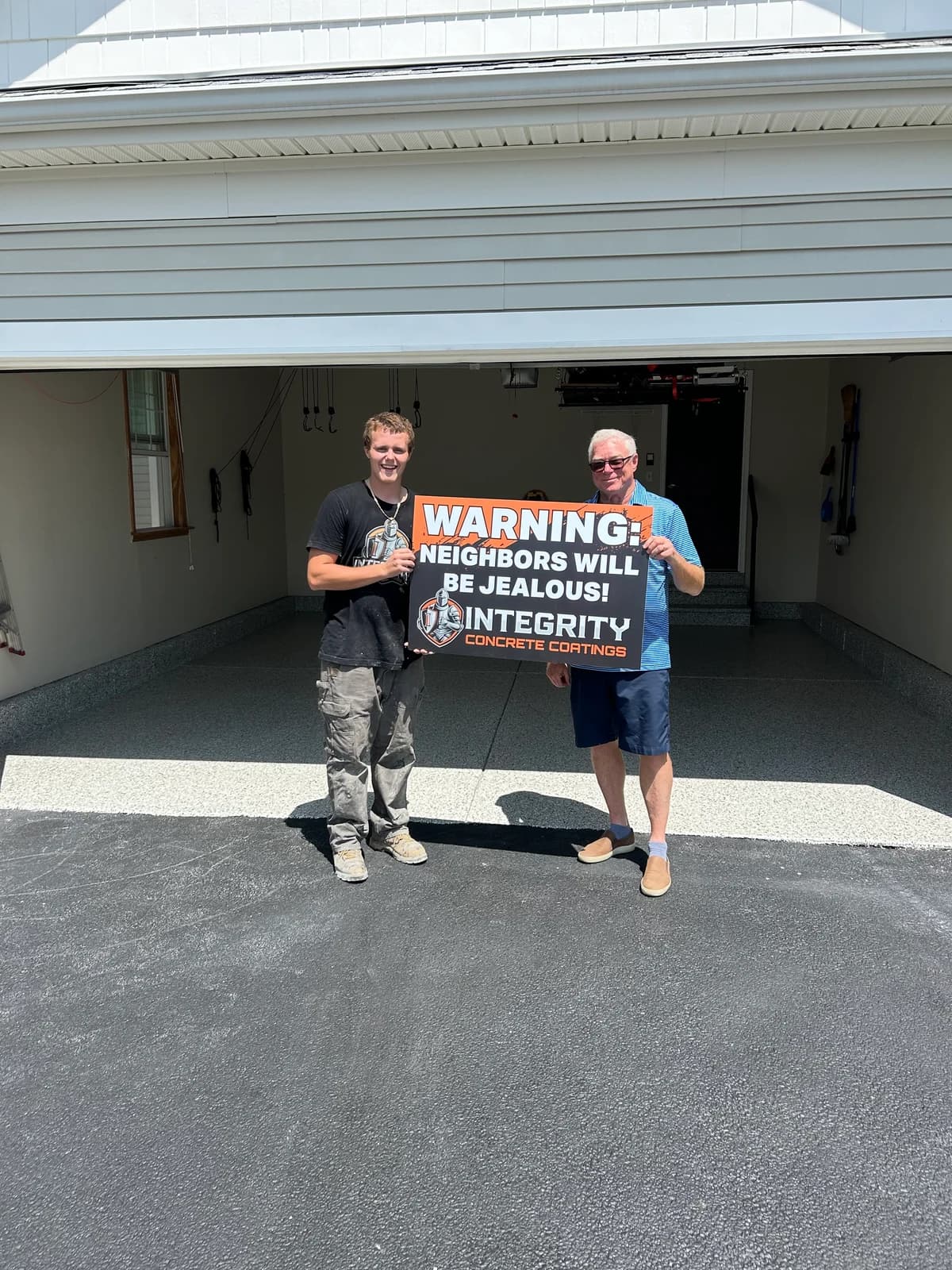 Crew member and homeowner holding a Neighbors Will Be Jealous sign at a white garage