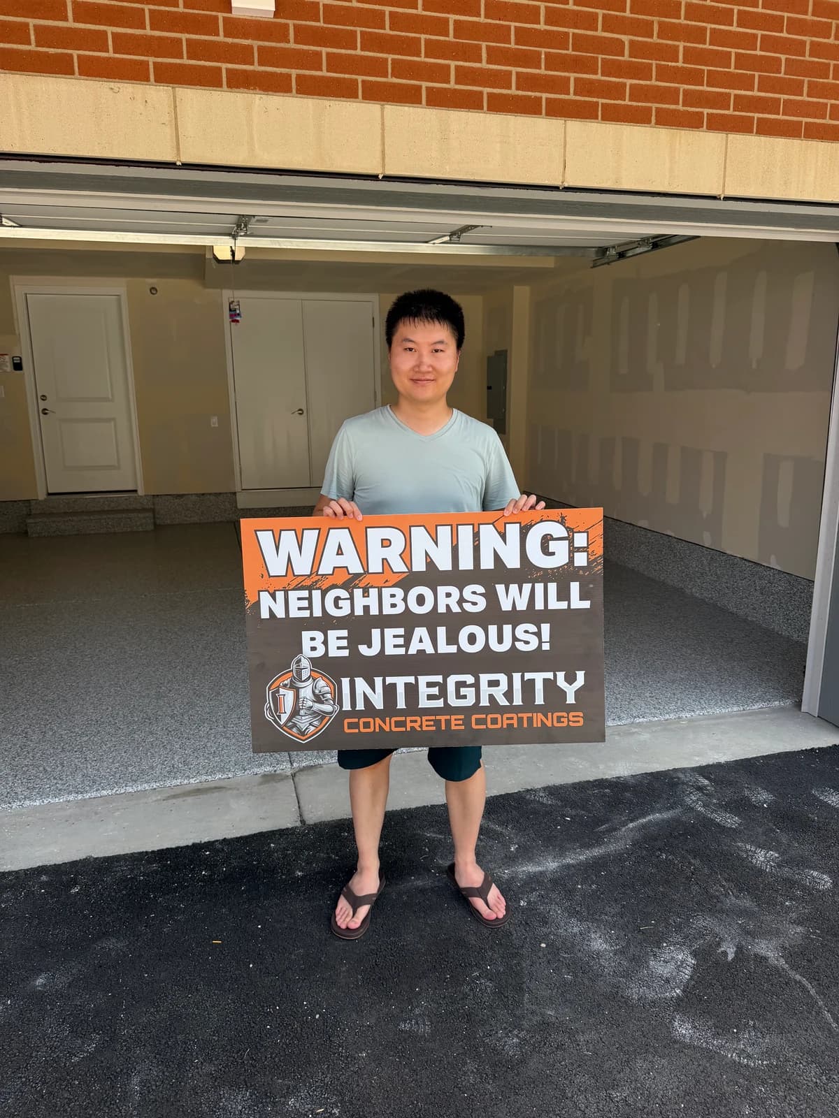 Customer holding a Neighbors Will Be Jealous sign at a brick home garage with flake coating