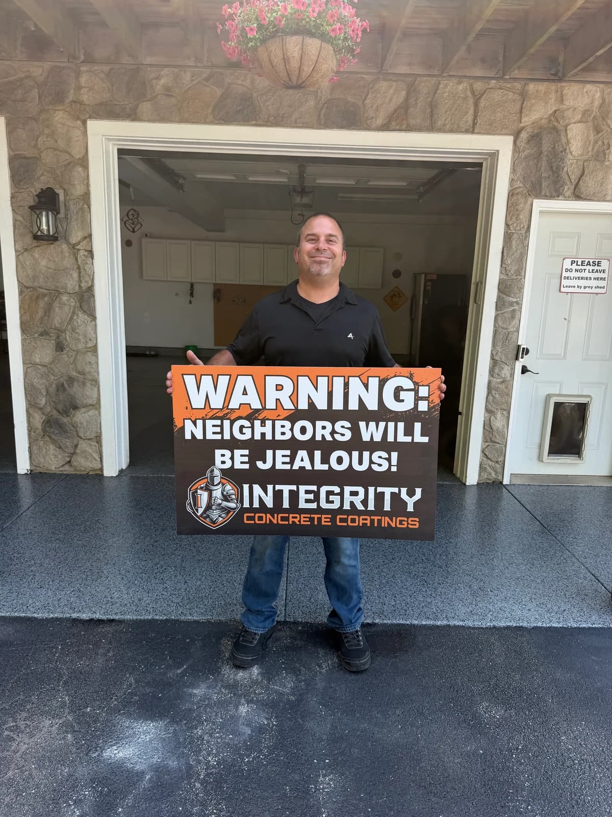 Customer with a Neighbors Will Be Jealous sign outside a stone facade garage with a coated floor