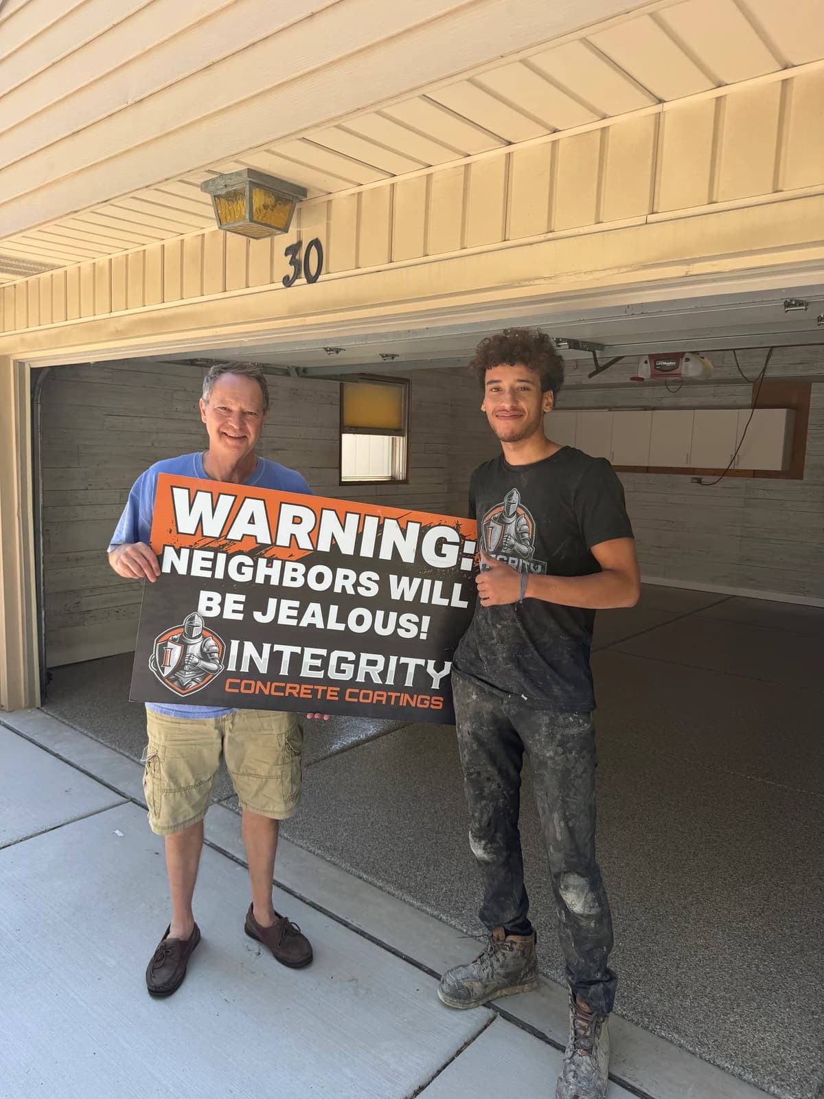 Homeowner and crew member with a Neighbors Will Be Jealous sign at a coated garage