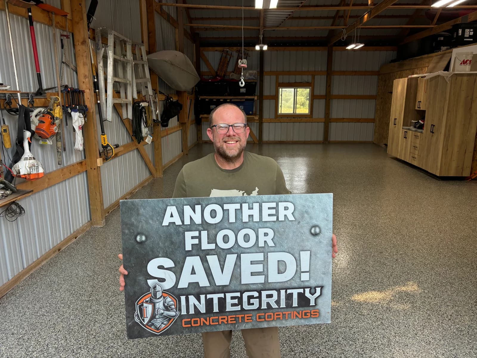 Customer holding an Another Floor Saved sign inside a pole barn with a coated concrete floor