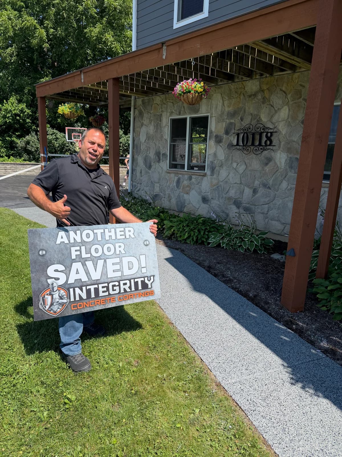Customer holding an Another Floor Saved sign beside a newly coated concrete walkway
