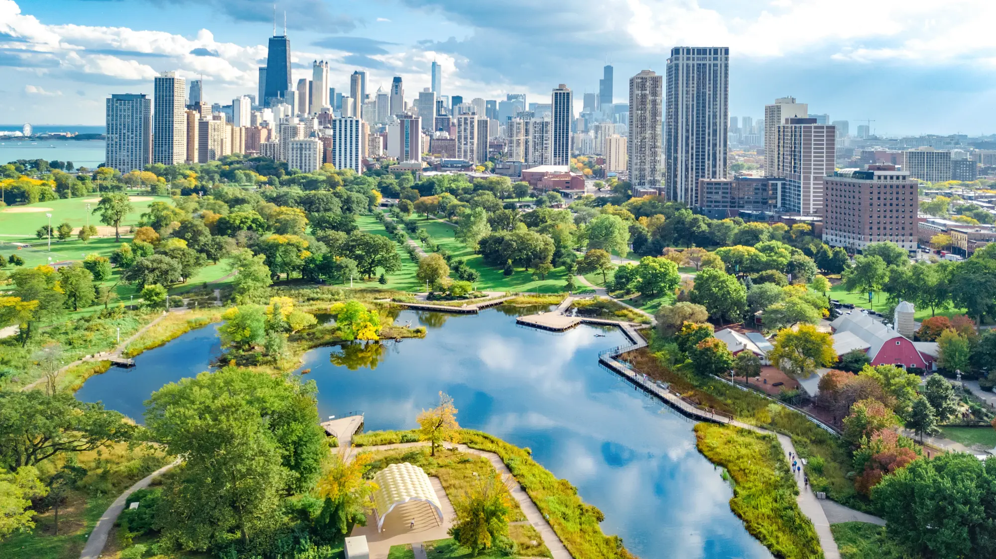 Aerial view of the Chicago skyline beyond a park lagoon and tree-covered parkland
