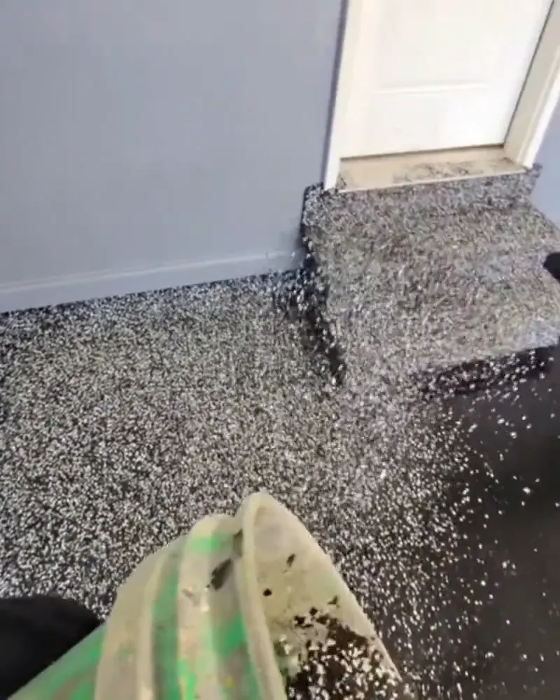 Rolling the polyurea base coat and broadcasting flake across a garage floor