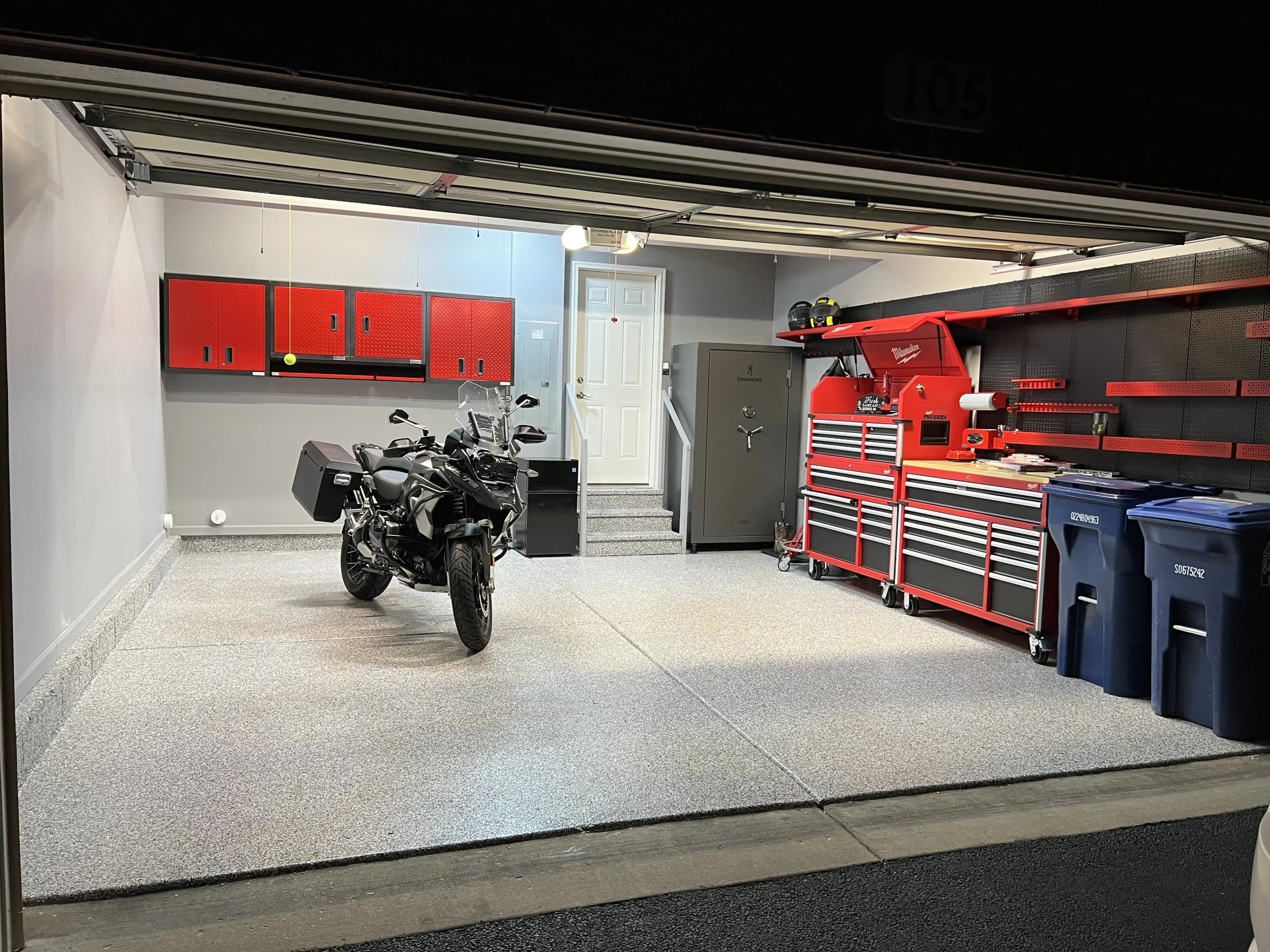 Residential garage at night with the door open, a light gray flake floor, a motorcycle and a red tool chest along the wall